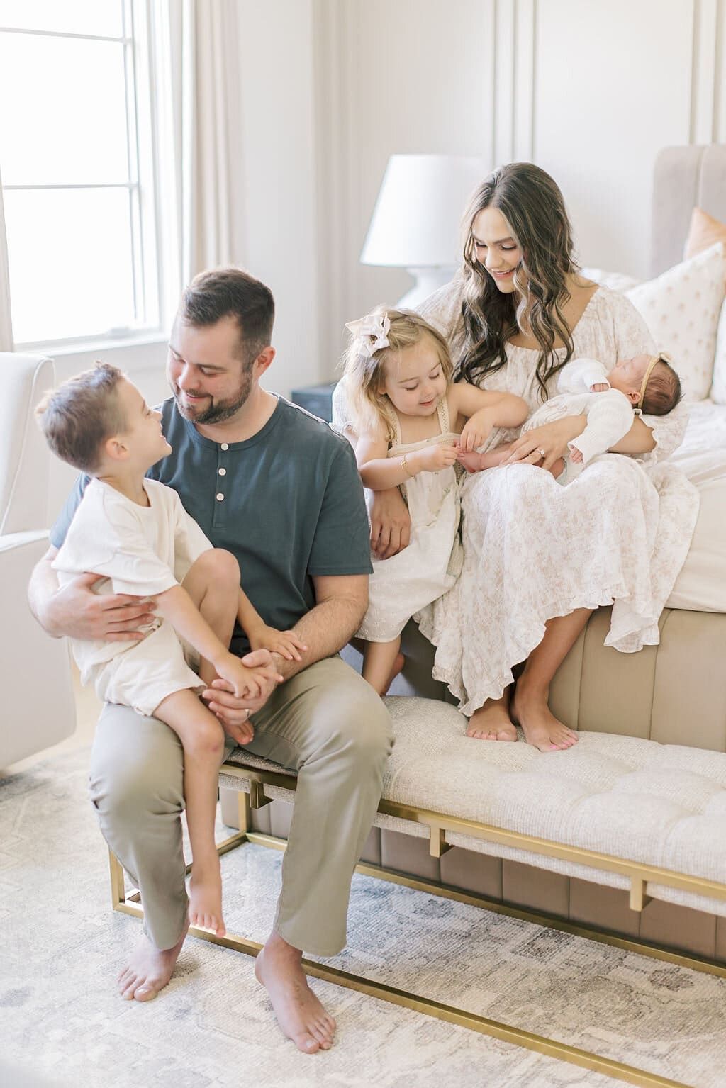 Family of five snuggling on the bed during an in-home Raleigh newborn session, with older siblings gently admiring their new baby sister.