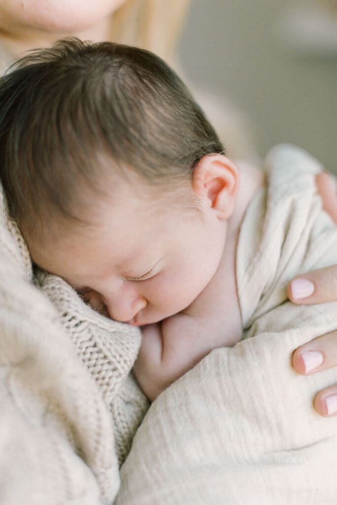 Peaceful close-up of a sleeping newborn snuggled against mama’s sweater during an intimate Raleigh newborn photography session.