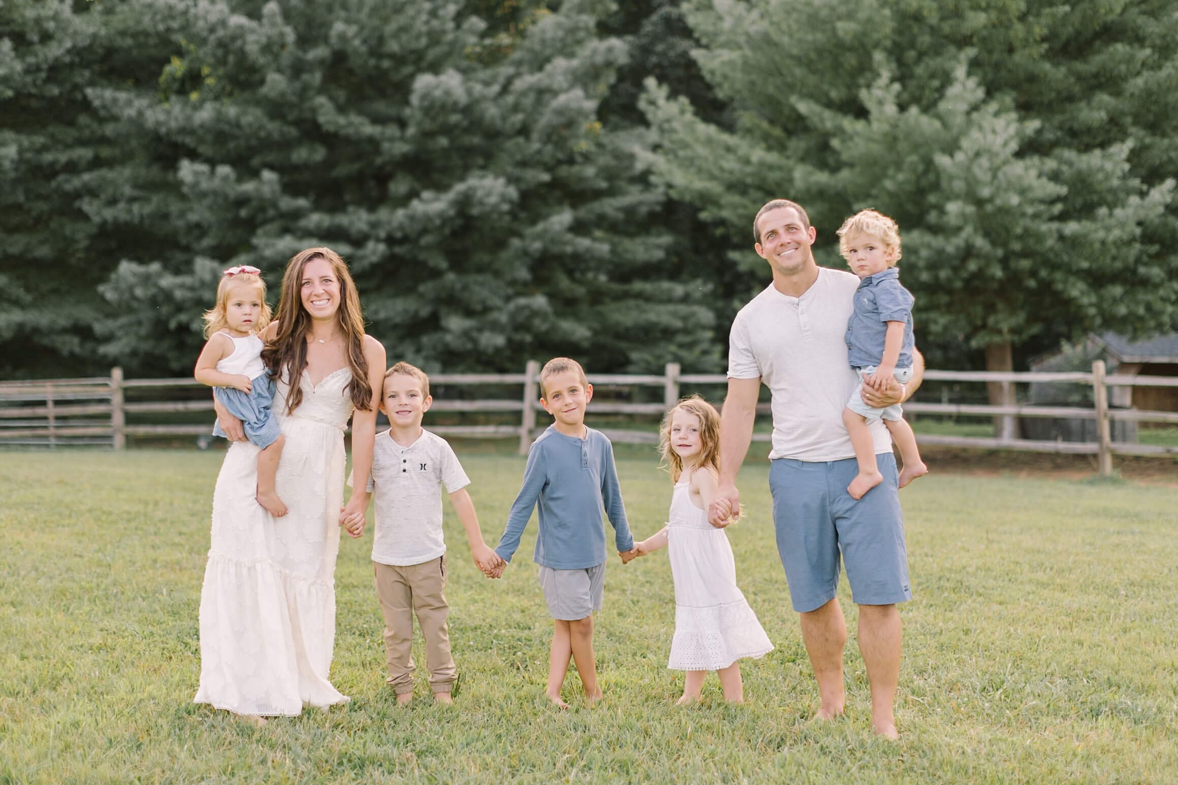 A happy large family with 5 young children walk in a pasture holding hands and smiling