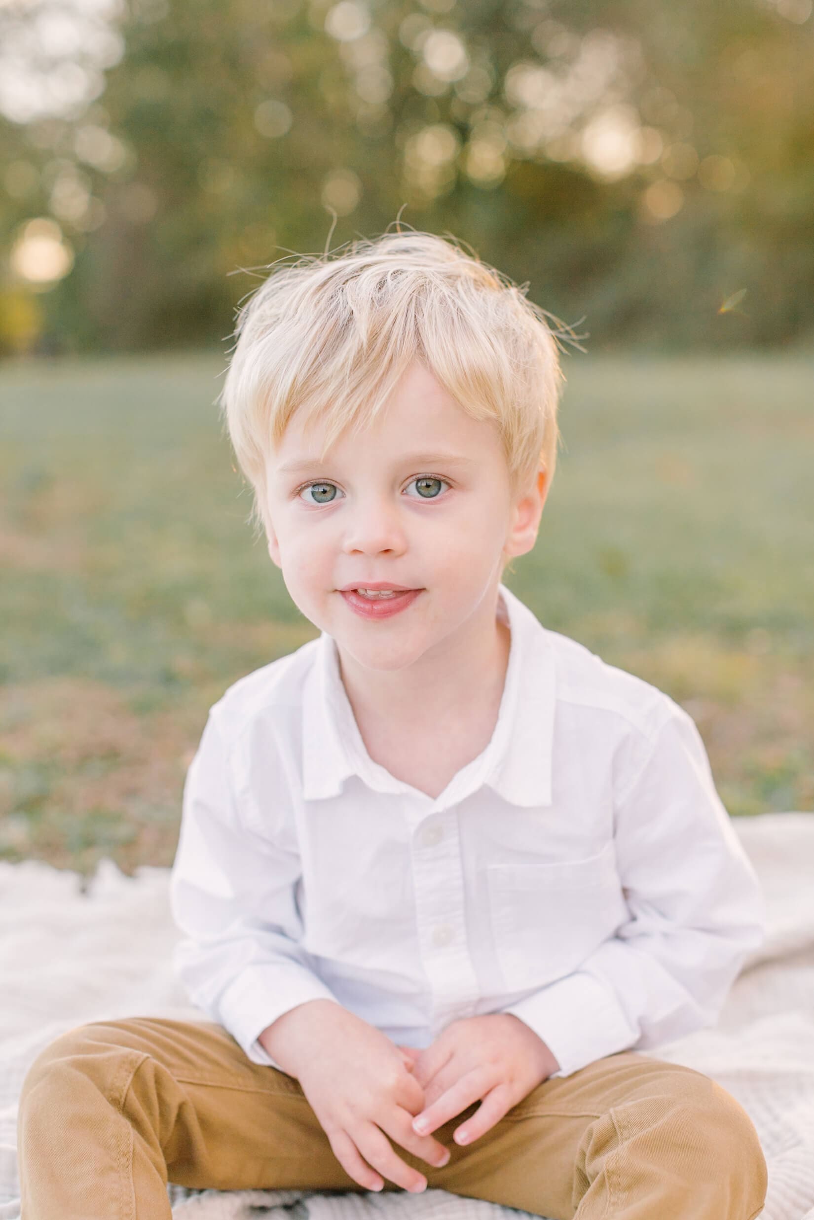 A young boy sits on a picnic blanket in a white shirt and khaki pants