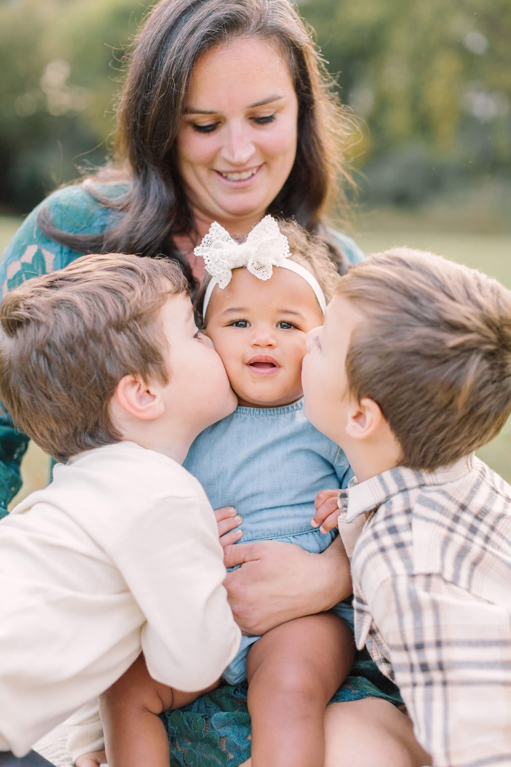 Young brother kiss the cheeks of their infant baby sister being held by mom