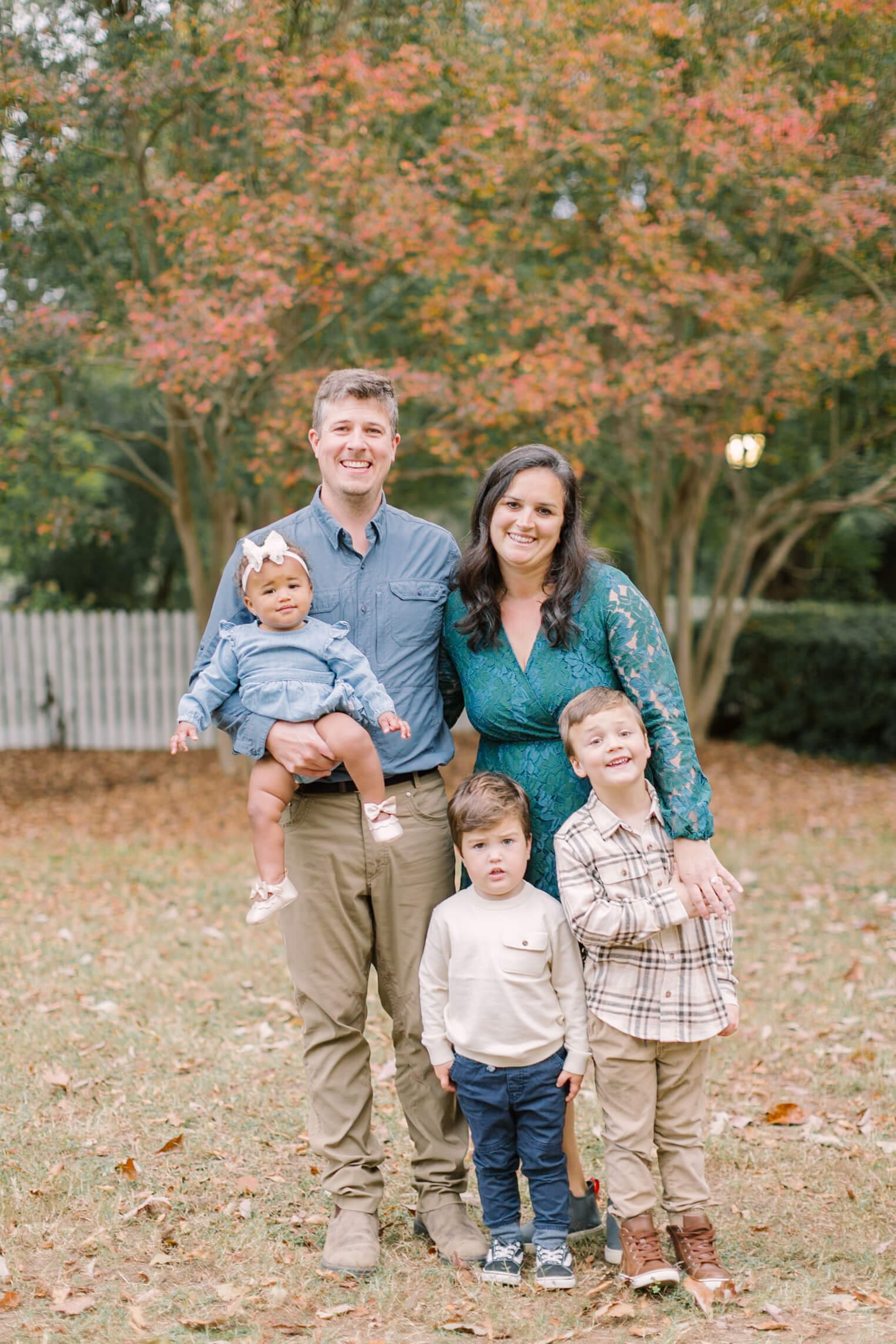 Happy mom and dad stand in the lawn smiling with their three young children during some fall activities in raleigh