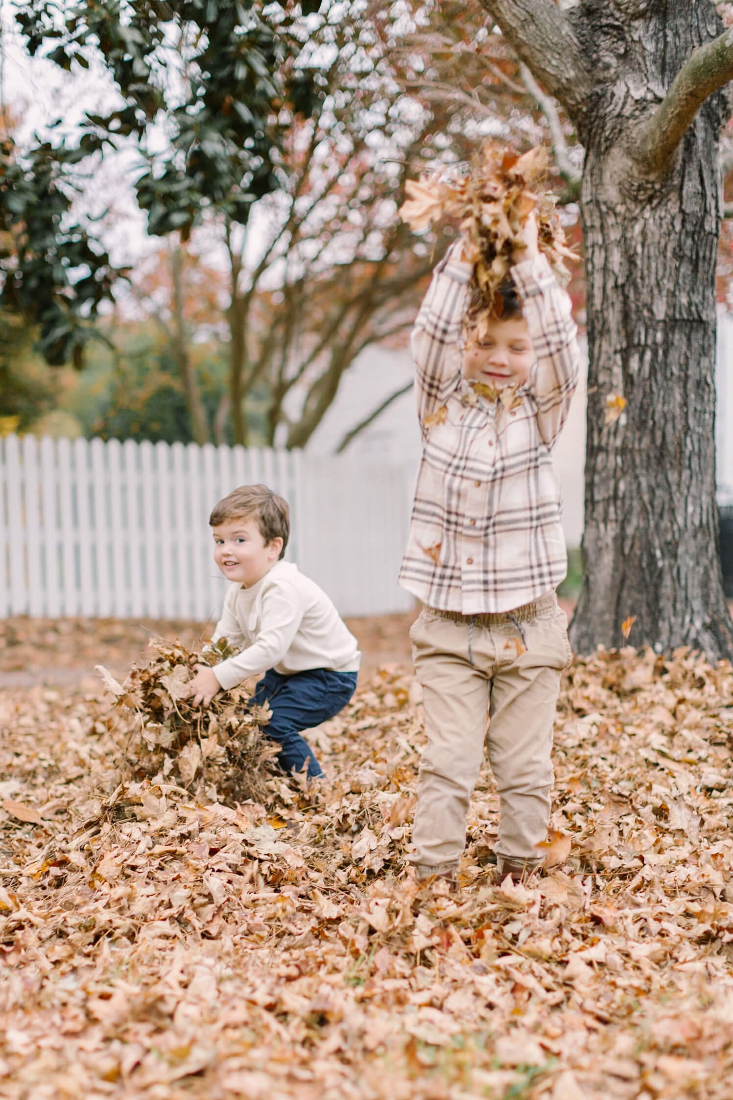 Two brothers in tan shirts play in some leaves in the yard during some fall activities in raleigh