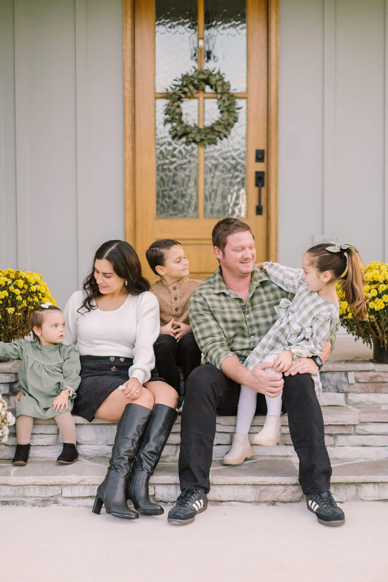 A happy family sits on their porch steps cuddling and smiling together before heading out to fall festivals in raleigh
